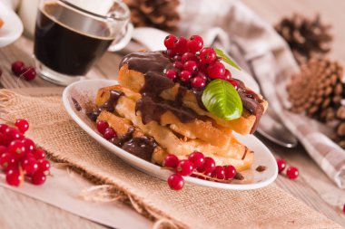 Waffle with red currant and chocolate topping on white dish.
