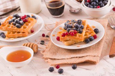 Waffles with red currant and blueberries on white dish.