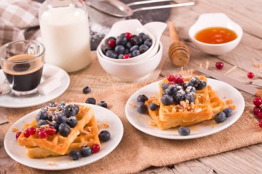 Waffles with red currant and blueberries on white dish.