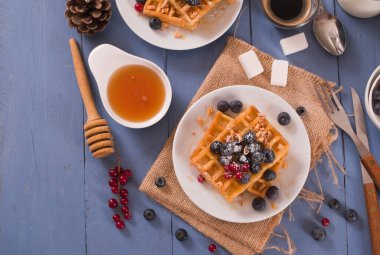 Waffles with red currant and blueberries on white dish.