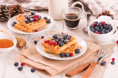 Waffles with red currant and blueberries on white dish.