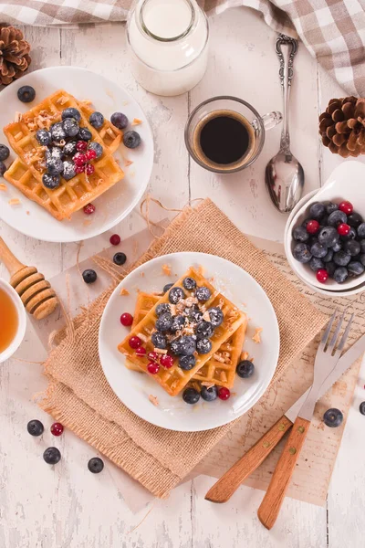 Waffles with red currant and blueberries on white dish.