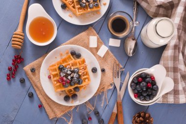 Waffles with red currant and blueberries on white dish.