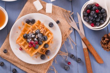 Waffles with red currant and blueberries on white dish.