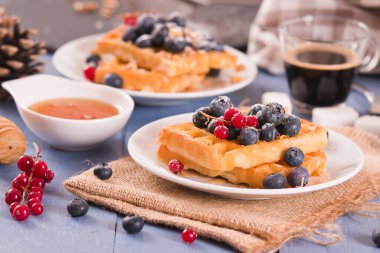 Waffles with red currant and blueberries on white dish.