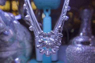 Yakın plan gümüş boncuklu iplikler turkuaz bir stantta asılı, bulanık arka plan.