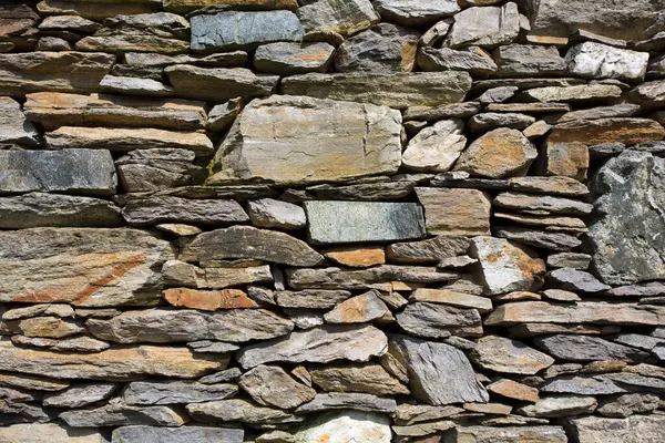 Değişen boyut ve renklerden oluşan yatay olarak istiflenmiş desenli taş bir duvar..