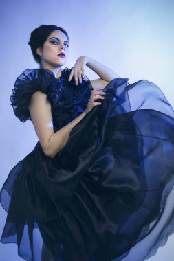 Çarşamba günü kostümcü kız Adams 'ın siyah elbisesi stüdyoda mavi ışık altında poz veriyor.