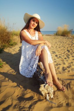 Kumsalda oturan şapkalı güzel bir kadın. Kum tepecikleri desenli bir fotoğraf.