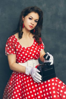 Güzel bir poster kızı, arka plandaki karanlık stüdyodan eski bir telefondan birini arıyor.