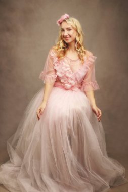 Çiçekli ve uyumlu başlıklı güzel, dalgalı pembe bir elbise giyen bir kadının göz alıcı bir stüdyo portresi. Bu görüntü moda, güzellik veya özel durum içeriği, zarafet ve neşe için idealdir..