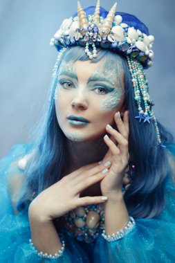  Deniz kabuğu tacı ve mavi makyajlı bir deniz kraliçesi olarak ruhani bir güzellik. Fantezi portresi güzellik, moda veya okyanus temalı projeler için mükemmeldir.