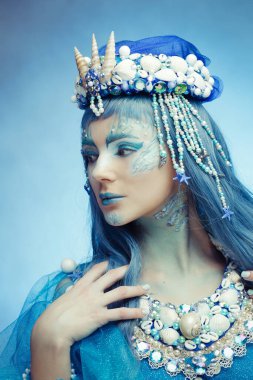  Karmaşık deniz kabuğu tacı ve mavi makyajlı mistik bir deniz kraliçesinin yan portresi. Fantezi, güzellik ve okyanus temalı tasarımlar için mükemmel.