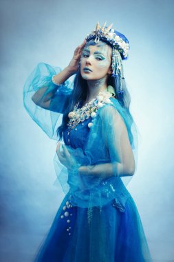 Rüya gibi bir pozda mistik mavi deniz kızı. Detaylı detaylarıyla okyanus kraliçesi ve dalgalı bir elbise. Denizin büyüsünü yakala.