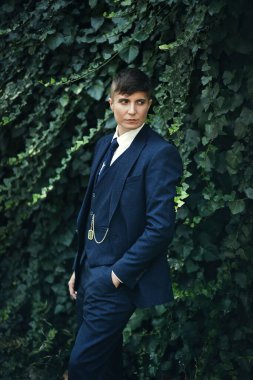 Androgynous zarafeti. İkili olmayan model, yemyeşil bir zemine karşı keskin bir takım elbiseye güvenir. Zamansız biçim modern kimlikle buluşur.