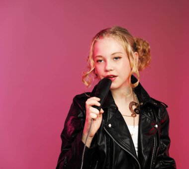 K-Pop / rocker tarzı giyinmiş, mikrofona şarkı söyleyen kendinden emin 10 yaşındaki bir kızın stüdyo çekimi. Pembe arka planda izole edilmiş..