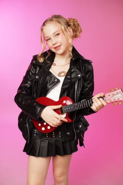 Oyuncak gitarlı 10 yaşındaki bir kızın pembe üzerine izole edilmiş eğlenceli bir fotoğraf stüdyosu fotoğrafı. Reklamlar, yazı işleri ve daha fazlası için mükemmel.