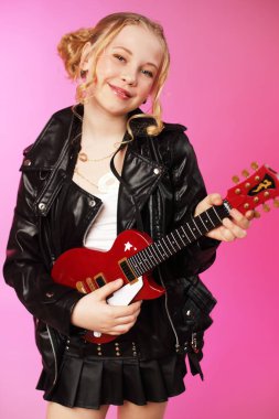 Oyuncak gitarlı 10 yaşındaki bir kızın pembe üzerine izole edilmiş eğlenceli bir fotoğraf stüdyosu fotoğrafı. Reklamlar, yazı işleri ve daha fazlası için mükemmel.