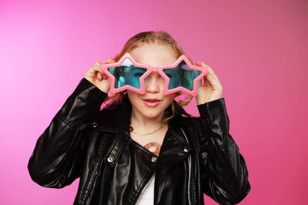 Крупный план портрета крутой 10-летней девочки, смотрящей на верх розовых звездных солнцезащитных очков на розовом фоне. Вдохновение в стиле К-поп