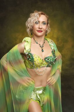 Karmaşık detaylı zümrüt yeşili kostümlü kendinden emin bir dansçının çarpıcı portresi. Kültür ve performans temaları için mükemmel.