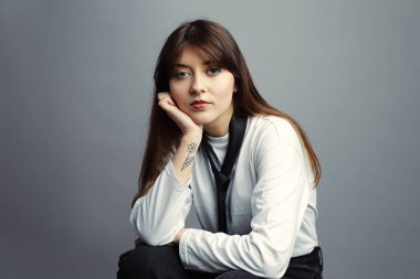 Sakin ve kendinden emin genç bir kadının portresi. Çenesini eline dayayıp doğrudan kameraya bakıyor. Özgüven, sabır ve modern profesyonellik kavramı