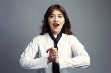 Diş teli takmış etkileyici genç bir kadın heyecanlı bir şekilde soluk soluğa, elleri sımsıkı, gözleri açık. Şık bir şekilde beyaz gömlek ve kravat giymişti. Gri stüdyo geçmişi.