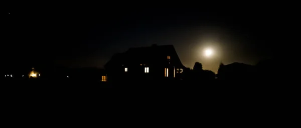 Wooden country house with light in the windows during a moonlit night.