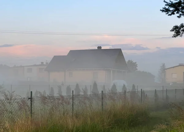 Rural landscape. A wooden log house surrounded by meadows and bushes shrouded in mist.