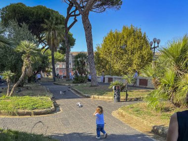 Çocuk parkta kaldırımda yürüyen güvercinlerin ve diğer kuşların peşinden koşar. Napoli, İtalya