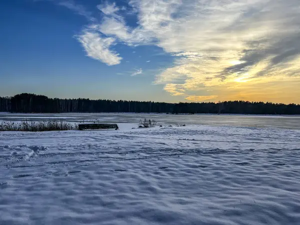 The sun setting over a snow-covered beach and a frozen pond. A boat pulled ashore is visible.