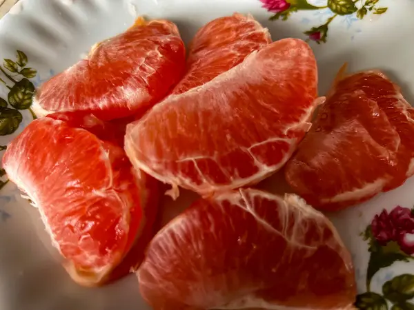 Pieces of peeled red grapefruits lying on a plate close-up.