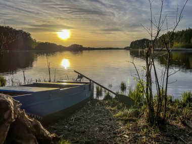 Sahilde görünen bir tekneyle gölün üzerinde gün batımı.