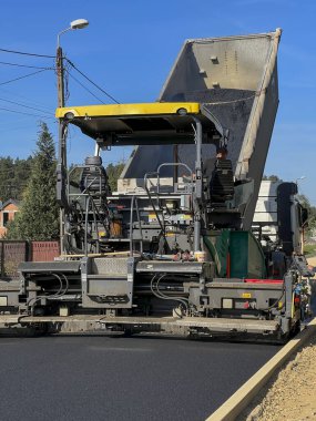 Yeni bir sokak yüzeyinin inşası. Uzman bir makineyle asfalt tabakası sermek.