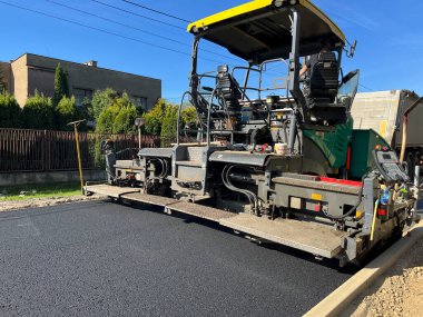 Yeni bir sokak yüzeyinin inşası. Uzman bir makineyle asfalt tabakası sermek.