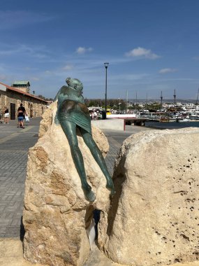 Paphos, Kıbrıs, 13 Ekim 2024: Kıbrıs Rum Kesimi 'nin Paphos limanında bir taşın üzerinde yatan bir kadın heykeli. Kalçalarını ellediği belli oluyor..