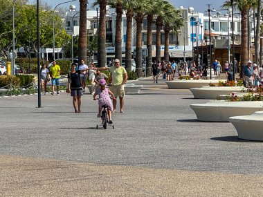 Paphos, Kıbrıs, 13 Ekim 2024: Kıbrıs Rum Kesimi 'nin Paphos limanı yakınlarındaki sahil boyunca gezinti alanı. Ebeveynler kızlarının üç tekerlekli bisiklete binmesinden hoşlanır..
