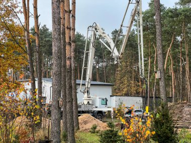 Kamyona monte edilmiş beton karıştırıcıyla beton dökerek, kendinden itişli bir pompa kullanarak, ağaçların arasında inşa edilen tek bir aile evi için temel şeritlerine beton dökerek..