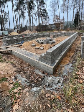 Construction of foundations for a single-family house made of four layers of concrete blocks on a cast concrete footing reinforced with steel rods. clipart