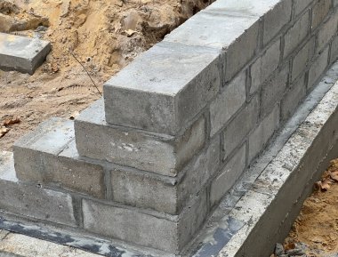 Construction of foundations for a single-family house made of four layers of concrete blocks on a cast concrete footing reinforced with steel rods. clipart