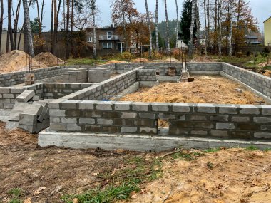 Construction of foundations for a single-family house made of four layers of concrete blocks on a cast concrete footing reinforced with steel rods. clipart