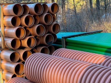 Kanalizasyon şebekesinin inşası sırasında yol kenarında depolanan yeşil ve kahverengi kanalizasyon boruları.