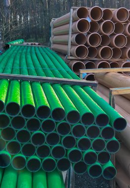Kanalizasyon şebekesinin inşası sırasında yol kenarında depolanan yeşil ve kahverengi kanalizasyon boruları.