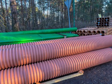 Kanalizasyon şebekesinin inşası sırasında yol kenarında depolanan yeşil ve kahverengi kanalizasyon boruları.