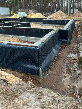 Çukurlu folyoyla kaplı tek bir aile evinin temelleri, neme karşı daha iyi bir yalıtım için kum ve toprak ile kaplanmaya hazır..