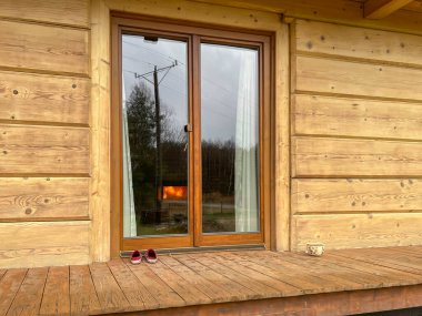 Dışarıdan görülebilen ahşap bir evdeki veranda penceresi. İçeride görünür bir şömine alevi var..