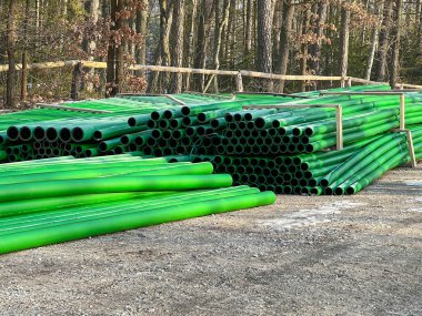 Kanalizasyon şebekesinin inşası sırasında yol kenarında depolanan yeşil ve kahverengi kanalizasyon boruları.