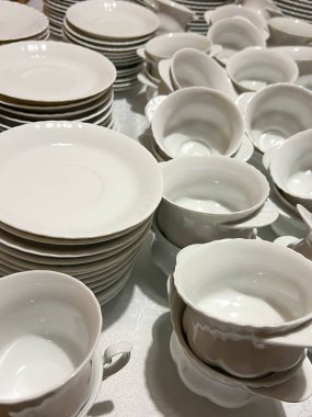 Bardaklar, tabaklar ve tabaklar masalara konmaya hazır beyaz ve gri renkli..