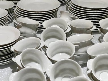 Bardaklar, tabaklar ve tabaklar masalara konmaya hazır beyaz ve gri renkli..
