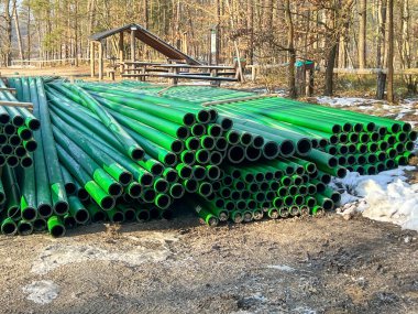 Kanalizasyon şebekesinin inşası sırasında yol kenarında depolanan yeşil ve kahverengi kanalizasyon boruları.