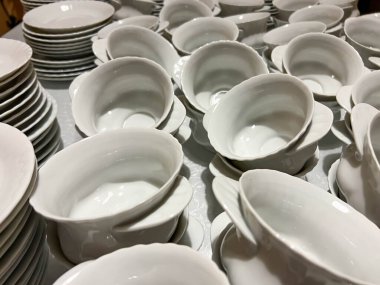 Bardaklar, tabaklar ve tabaklar masalara konmaya hazır beyaz ve gri renkli..